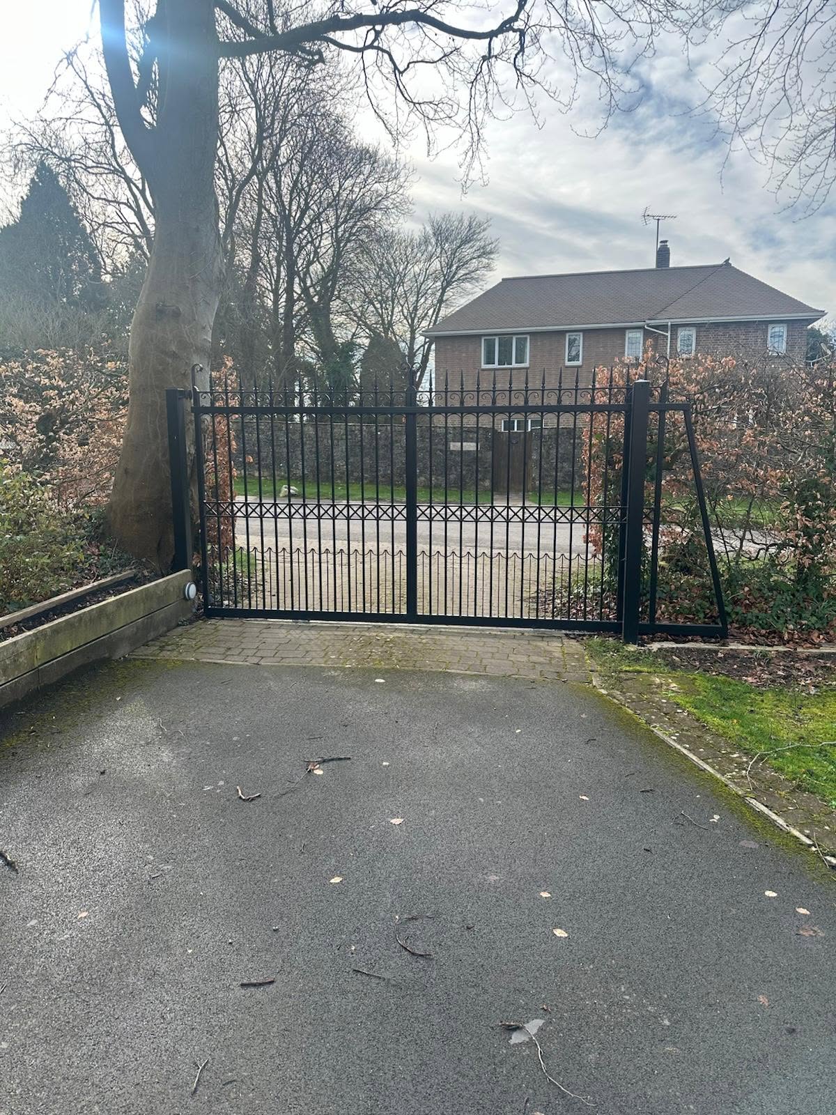 Traditional black wrought-iron driveway gates with spear-tip finials on a country property.