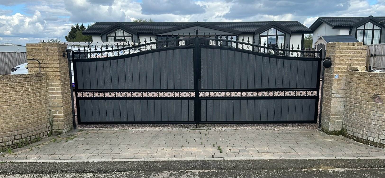 Low-profile arched black gates with grey infill and circular metal accents.