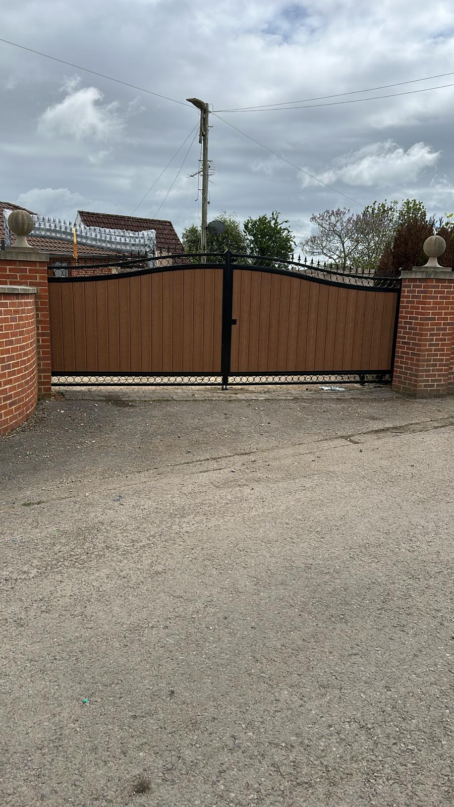 Arched black steel gates with brown composite infill between brick pillars.