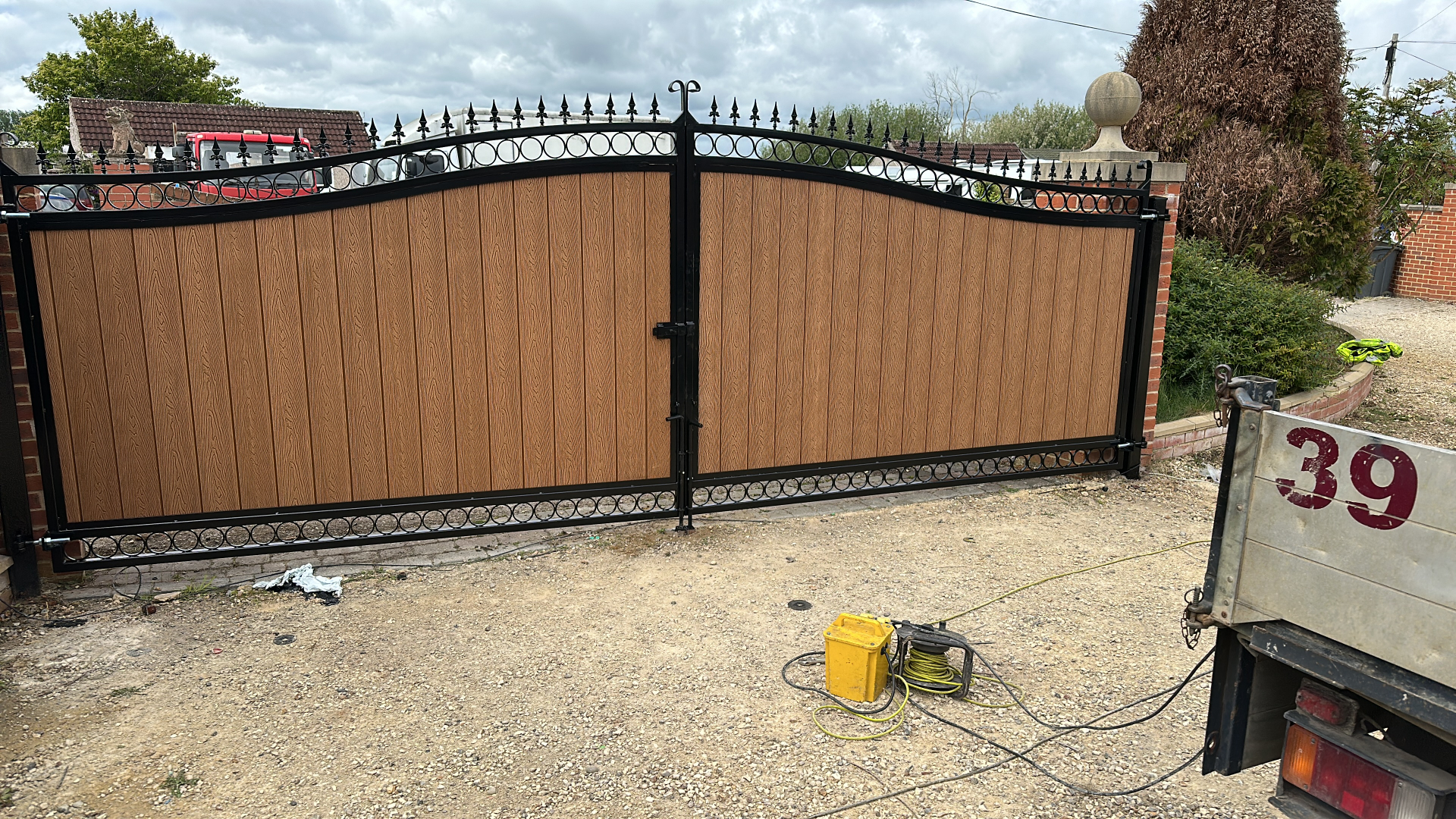 Arched black driveway gates with light brown composite infill.